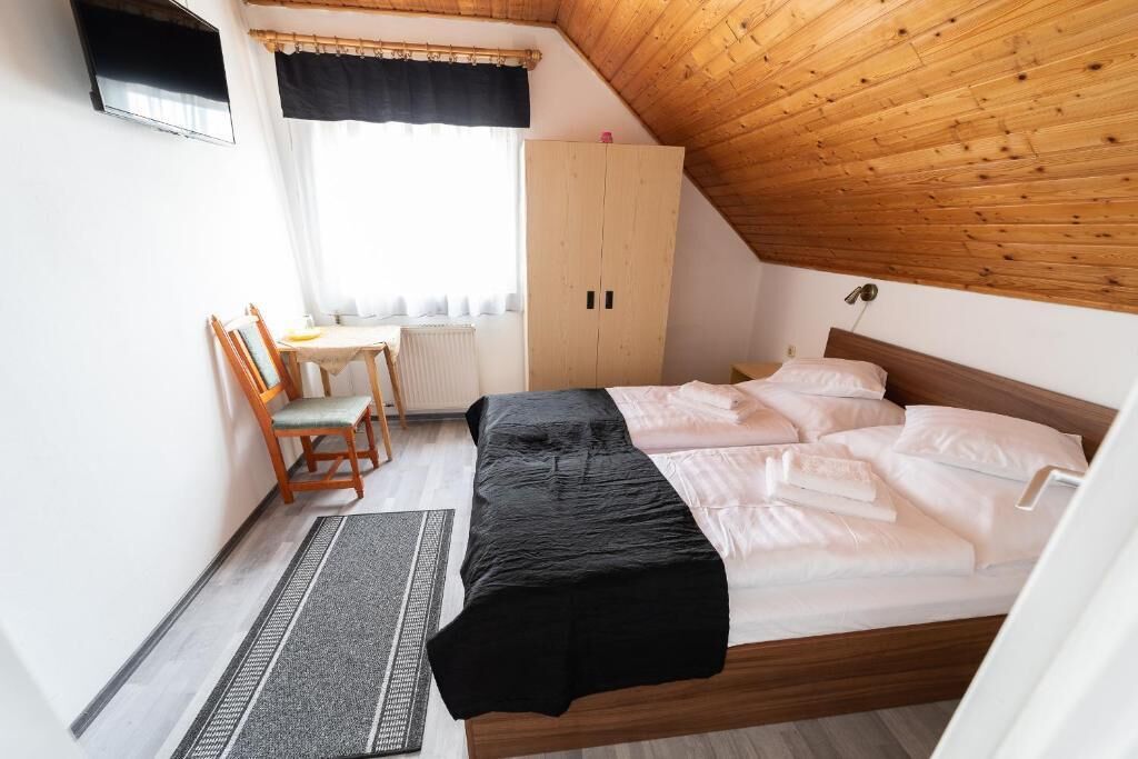 Ein Schlafzimmer mit Holzboden, einem Bett mit weißer Bettwäsche, einem Holzschrank, einem kleinen Tisch mit Stuhl und einem Fenster mit Vorhängen.