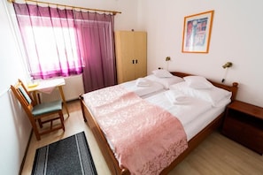 Un dormitorio con cama, un armario de madera, un escritorio con silla, una ventana con cortinas y un cuadro en la pared.