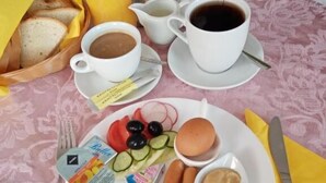 A breakfast setting with bread, juice, coffee, and a plate with eggs, ham, and vegetables. - VILLA LOTUS PANZIÓ (Zalakaros)