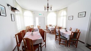A dining area with multiple tables and chairs, a chandelier, and framed pictures on the walls. - VILLA LOTUS PANZIÓ (Zalakaros)