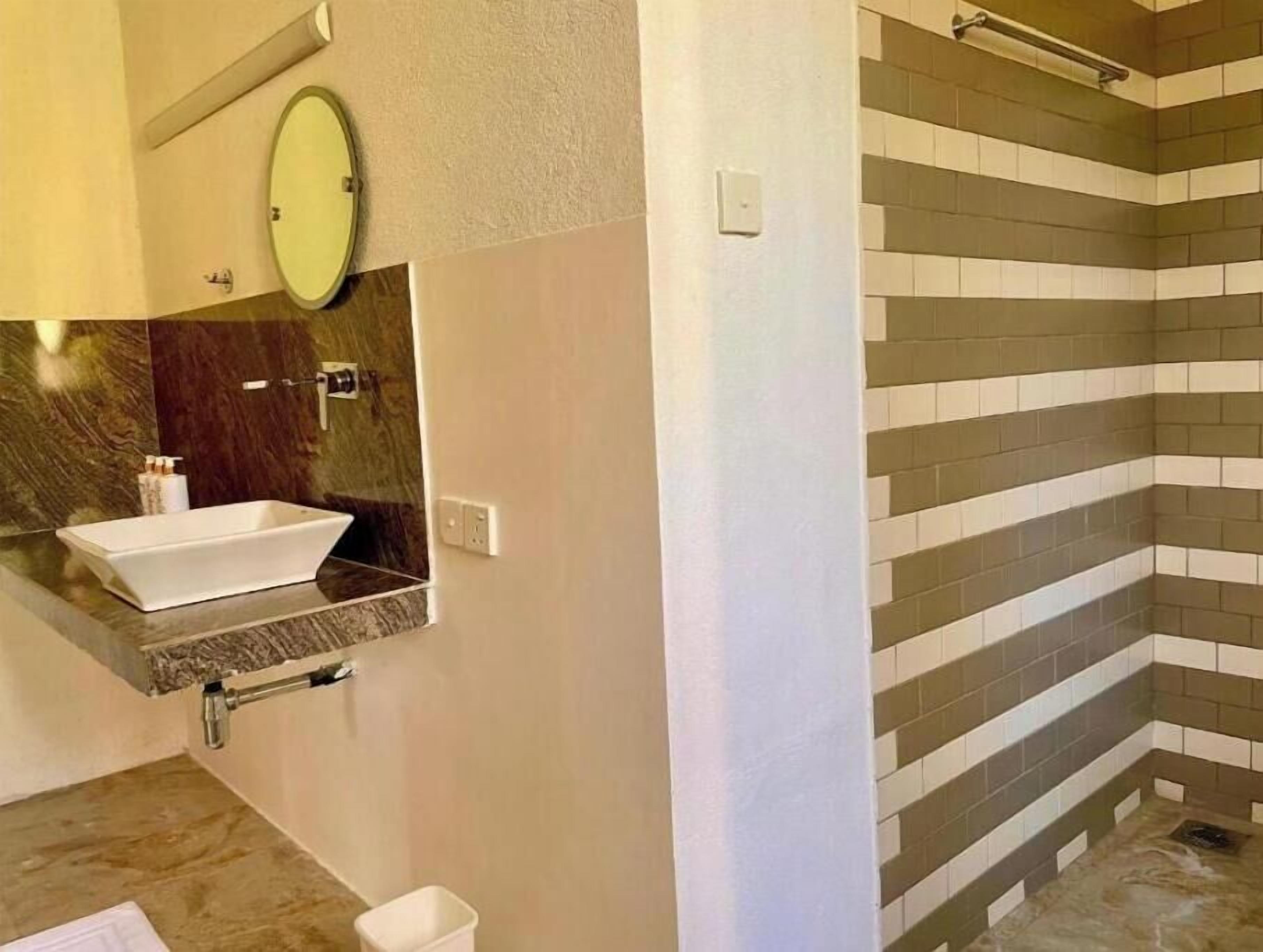 Une salle de bain avec un lavabo blanc, un miroir et une douche carrelée.