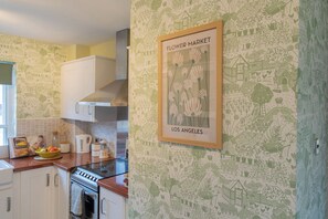 A kitchen with white cabinets, a stove, and a framed picture of flowers on the wall. - Sheriff's Tower Cottage - West (Bishop Auckland)