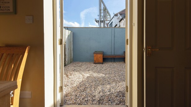An open doorway leading to a room with a gravel floor, a wooden bench, and a metal structure in the background. - Sheriff's Tower Cottage - West (Bishop Auckland)