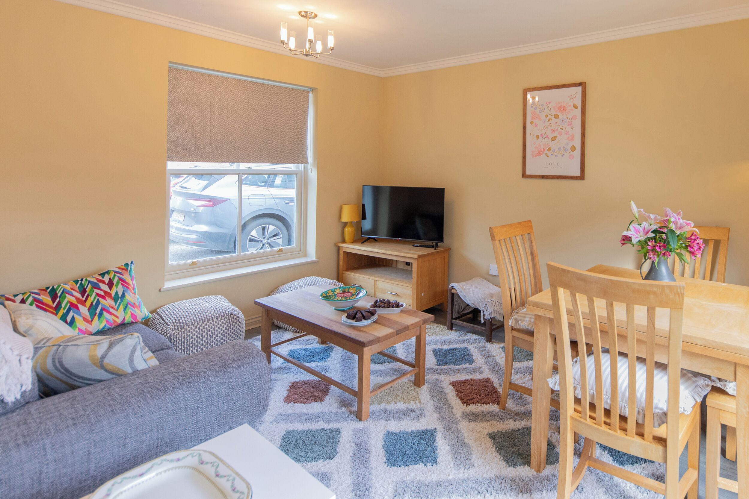 A living room with a sofa, a coffee table, a TV, and a dining table with chairs.