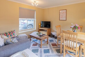 A living room with a sofa, a coffee table, a TV, and a dining table with chairs. - Sheriff's Tower Cottage - West (Bishop Auckland)