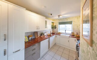 Una cocina con armarios blancos, encimera de madera, un lavamanos y una ventana con vista a la calle.
