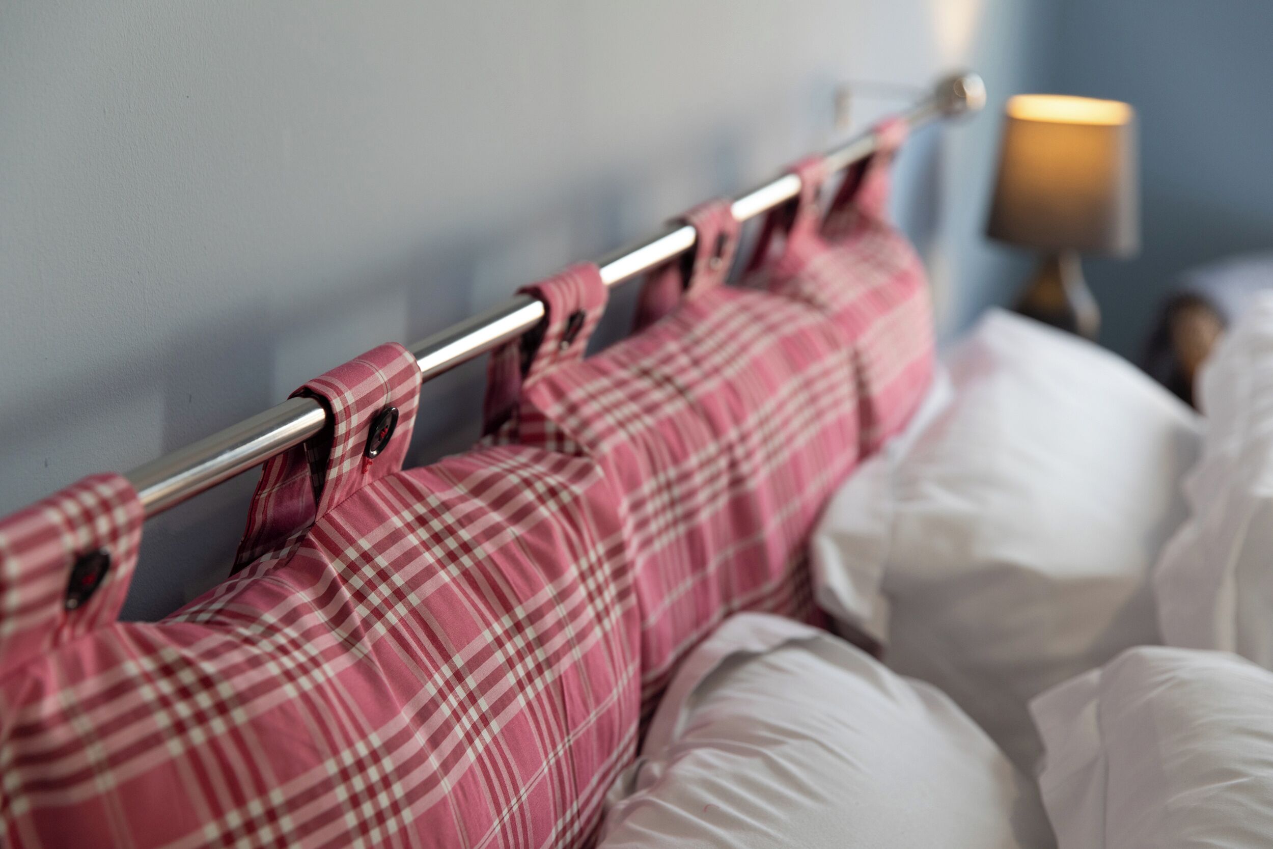 Ein Bett mit Metallkopfteil, rosa-weißer Bettwäsche und einer Nachttischlampe.