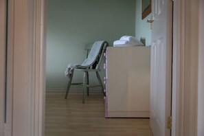 A room with a wooden floor, a chair with a blanket, a white cabinet, and a door. - Sheriff's Tower Cottage - West (Bishop Auckland)