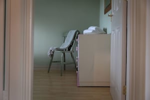 Una habitación con piso de madera, una silla con una manta, un armario blanco y una puerta.