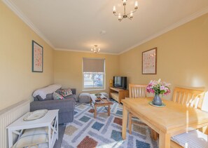 A living room with a sofa, a TV, a dining table, and a window. - Sheriff's Tower Cottage - West (Bishop Auckland)
