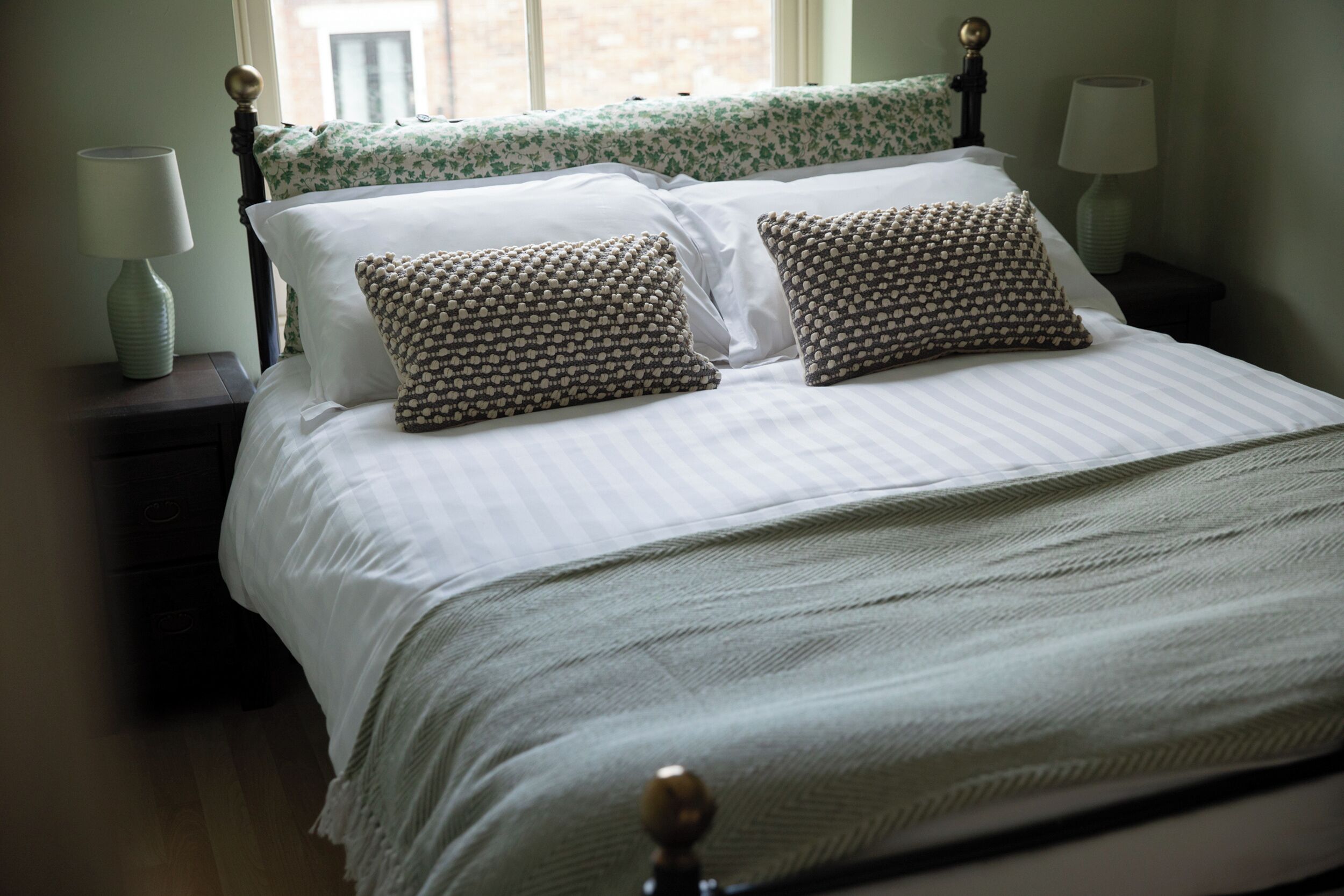 A neatly made bed with a checkered bedspread, two patterned pillows, and a wooden headboard.