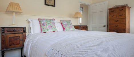 A bedroom with a bed, two bedside tables, a dresser, a door, and a wall-mounted lamp.