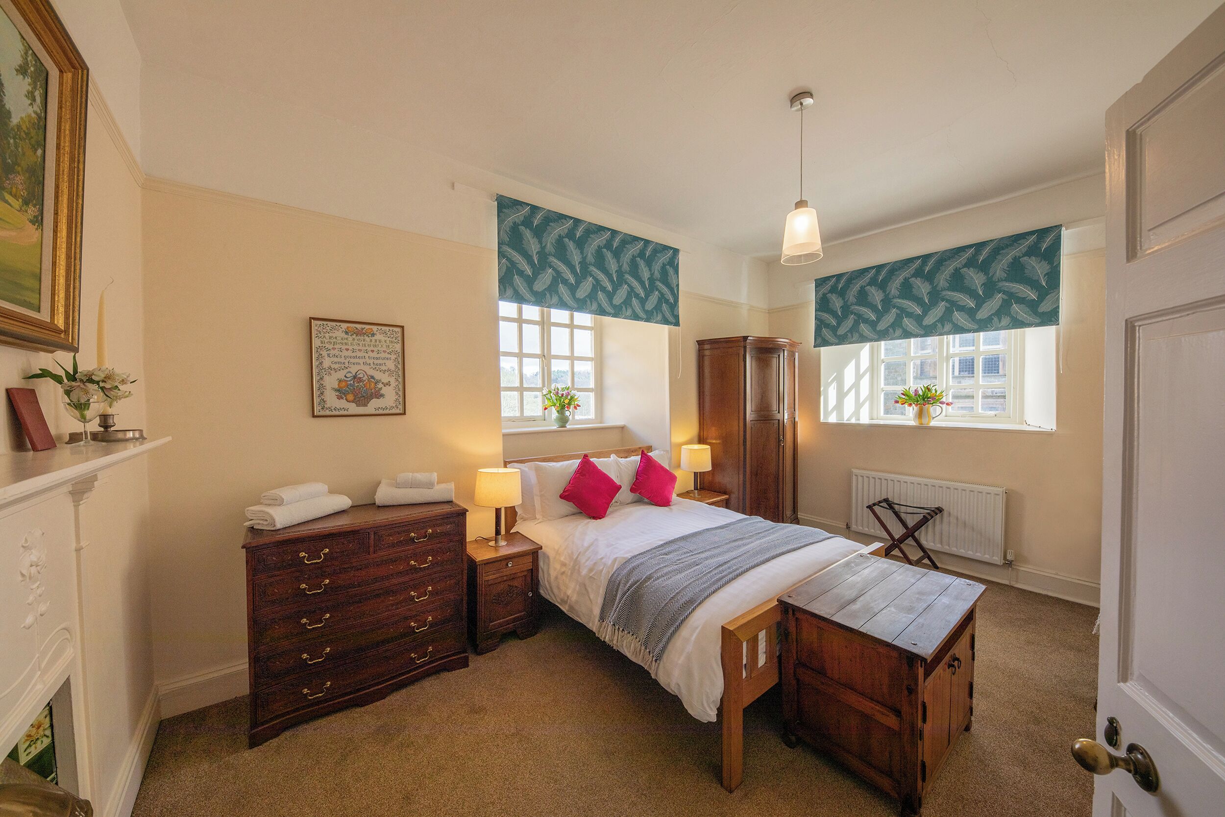 A bedroom with a bed, nightstands, a dresser, a bench, a radiator, and a window with a view.