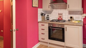 Una cocina con armarios blancos, estufa a gas, horno y pared roja.