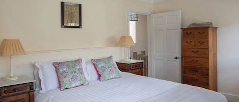 Een slaapkamer met een bed, twee nachtkastjes, een houten dressoir, een deur en een aan de muur hangend schilderij.