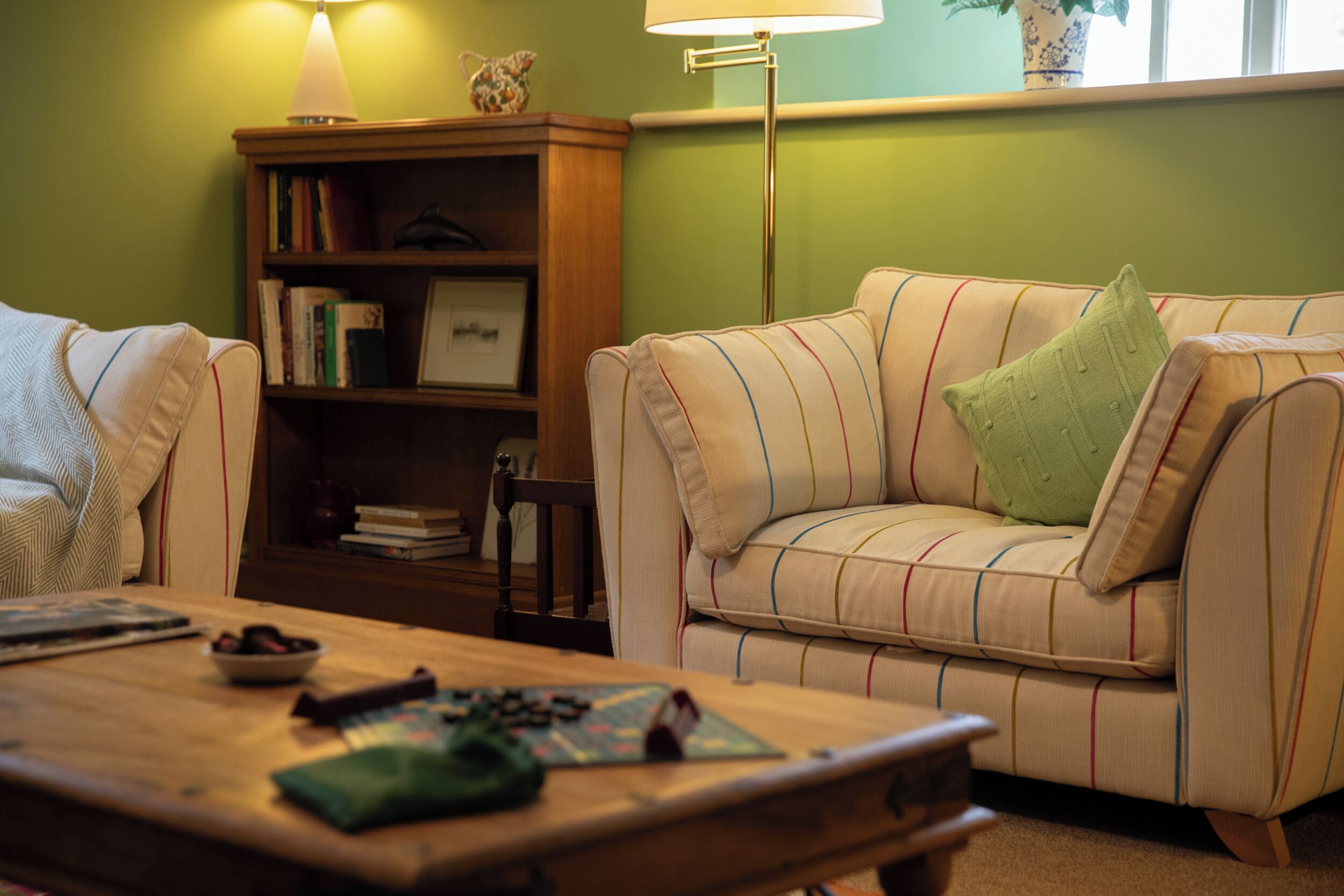 A cozy living room with a striped sofa, a wooden coffee table, and a bookshelf.