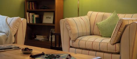 A cozy living room with a striped sofa, a wooden coffee table, and a bookshelf.