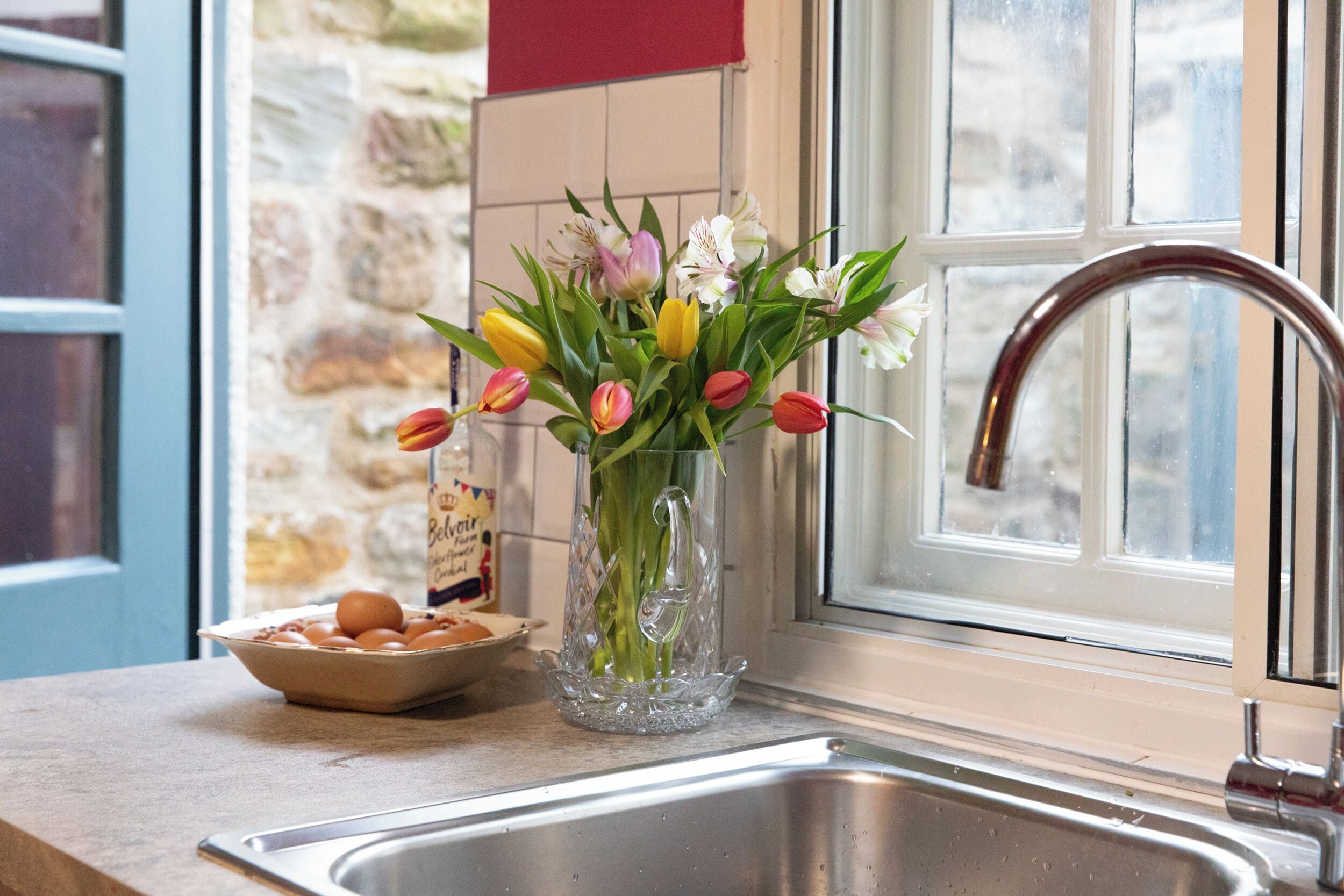 A kitchen with a sink, a vase with flowers, and a bowl of eggs.