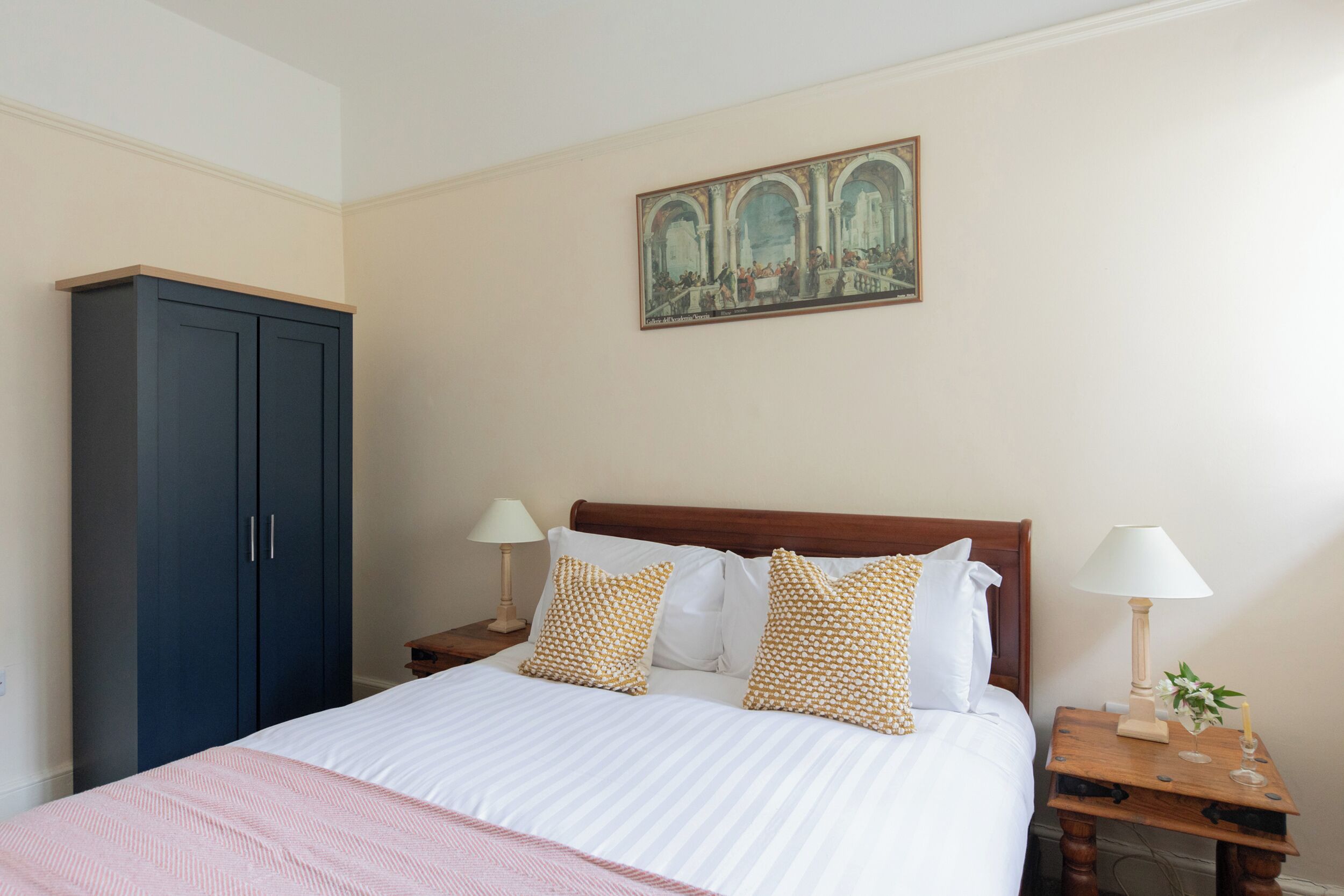A bedroom with a bed, two bedside tables, a wardrobe, and a painting on the wall.