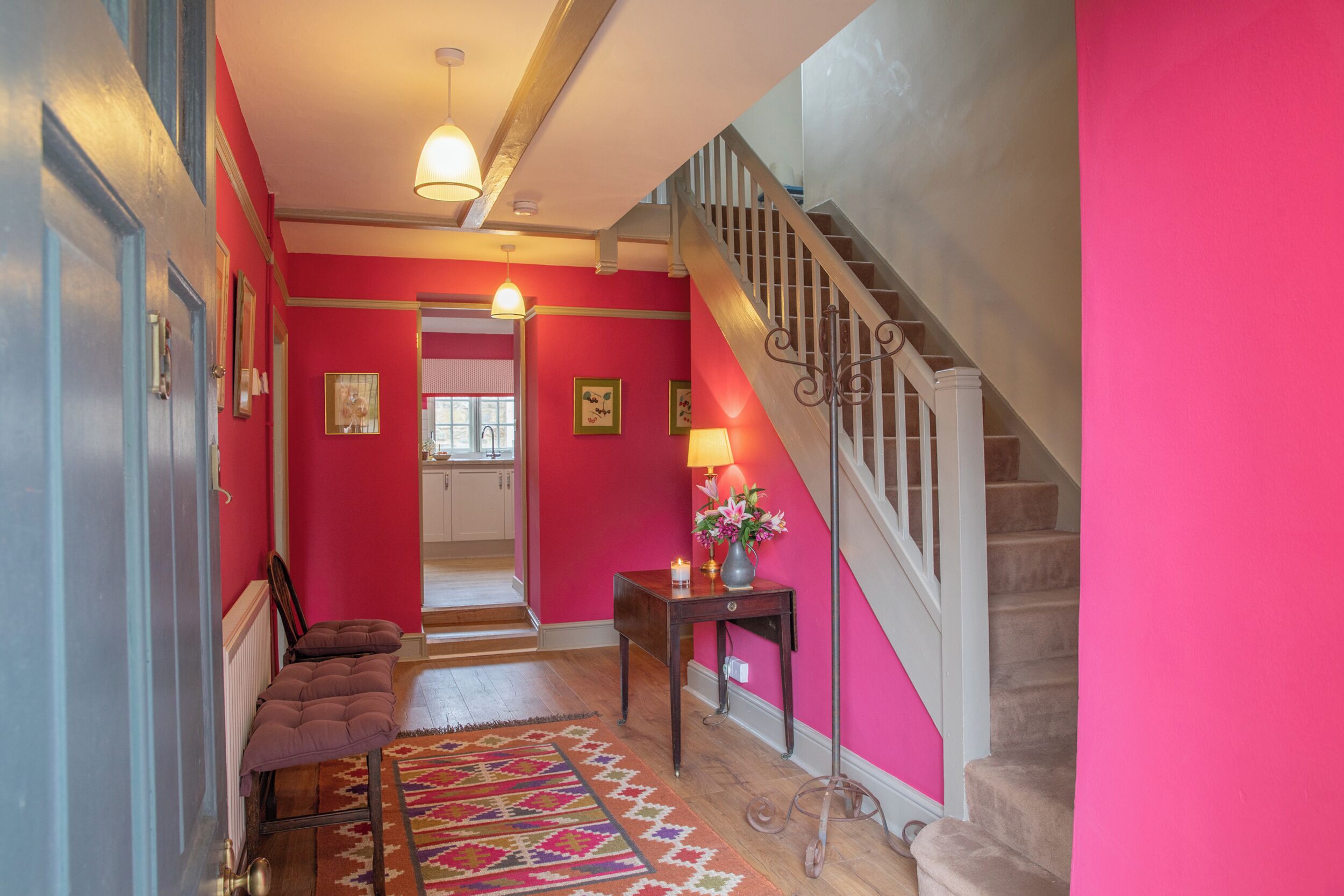 A hallway with a staircase, a radiator, a patterned rug, and a table with a lamp and flowers.