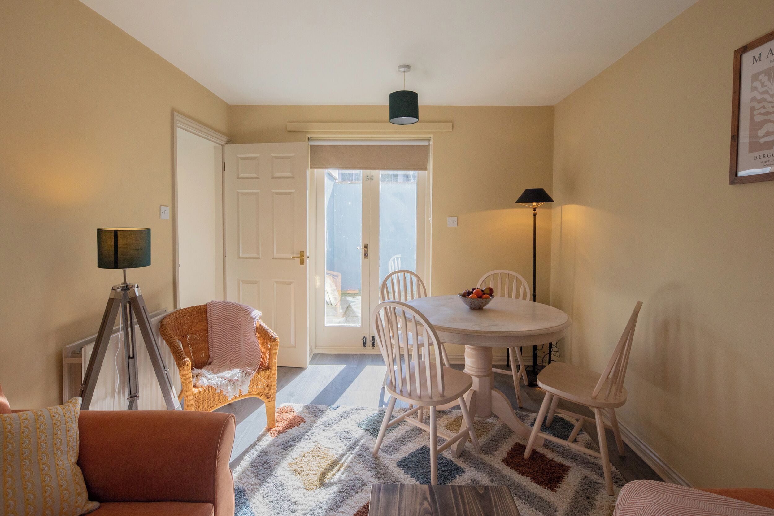 A dining area with a round table, white chairs, a floor lamp, and a door leading outside.