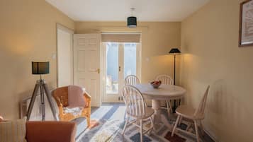 A dining area with a round table, white chairs, a floor lamp, and a door leading outside.