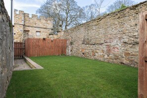 A stone wall, a wooden fence, and a grassy yard. - Sheriff's Tower Cottage - East (Bishop Auckland)