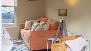 A cozy living room with a sofa, a floor lamp, a small table, and a wicker chair.