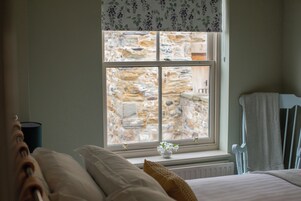 Un dormitorio con vista a una pared de piedra, una cama con almohadas, una mesita de noche y una silla.