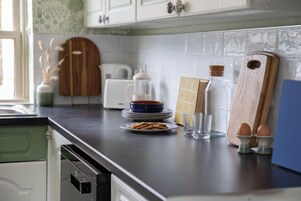 Una encimera de cocina con cafetera, platos, vasos y tabla de cortar.