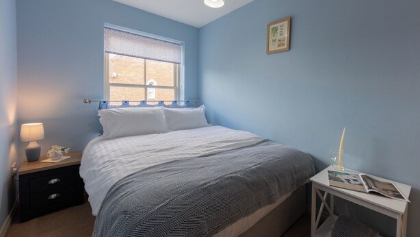 Quarto com cama, mesa de cabeceira, janela com vista e um quadro pendurado na parede.