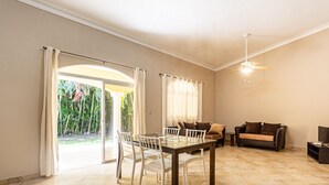 Uma sala ampla com uma mesa de vidro para refeições, dois sofás, um ventilador de teto e uma televisão.