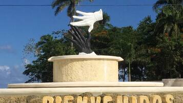 A welcome sign with a hand sculpture and palm trees in the background.