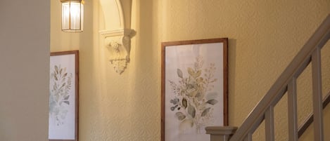 Una escalera con un accesorio de iluminación y una obra de arte botánica enmarcada en la pared.
