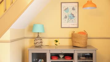 A corner with a grey cabinet, a blue lamp, a vase with yellow flowers, a woven basket, and a framed picture on the wall.