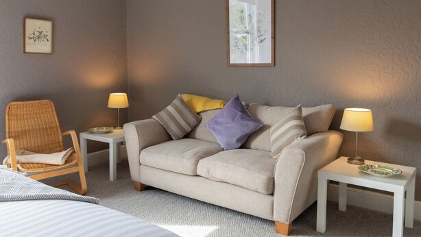 A neutral-toned room with a sofa, two side tables, a chair, and a bed. - No 2 Townhouse (Bishop Auckland)
