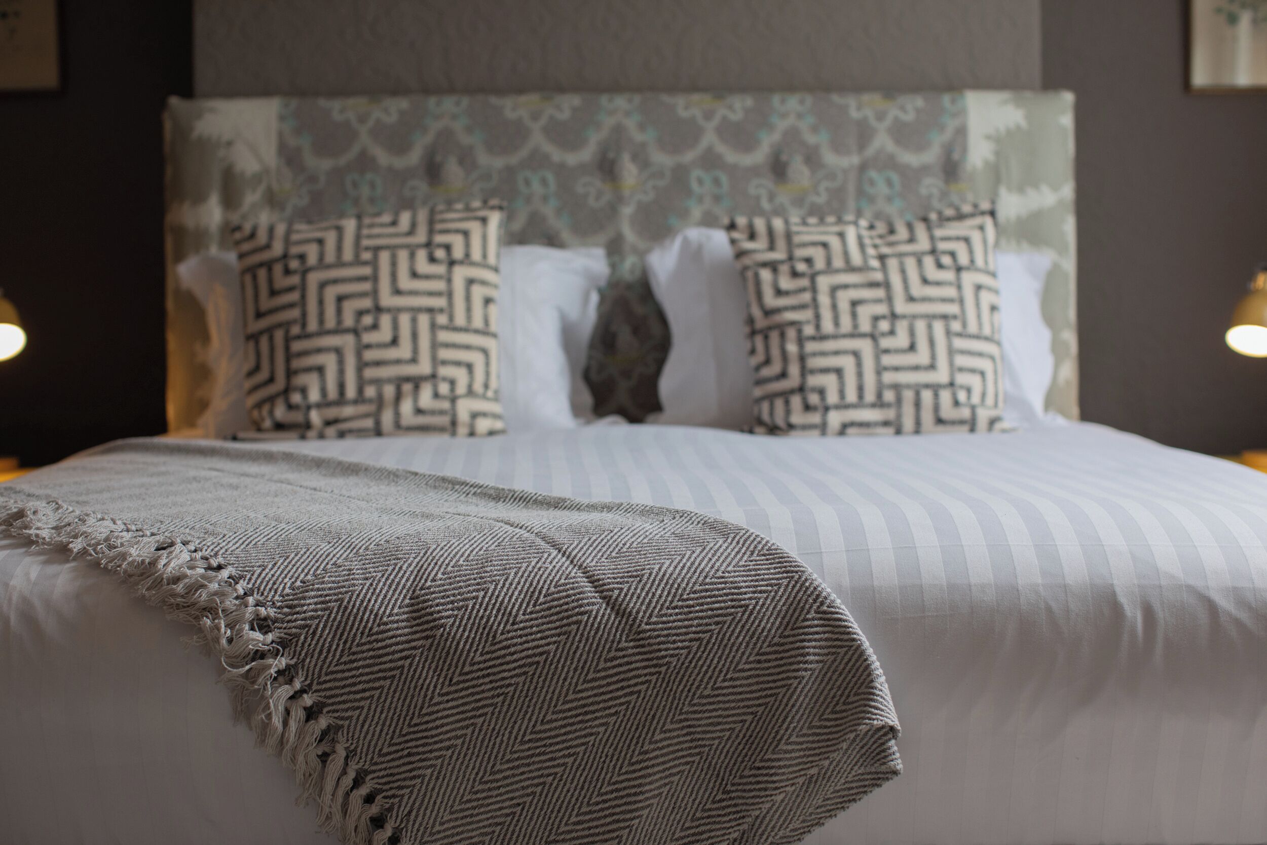 A neatly made bed with a patterned pillow, a striped blanket, and a headboard with a decorative design.