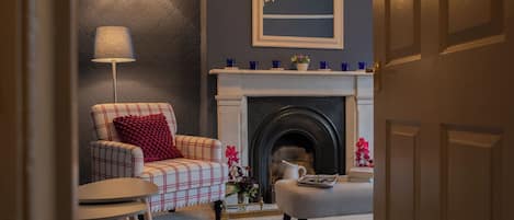 A living room with a fireplace, a plaid armchair, a lamp, and a coffee table.