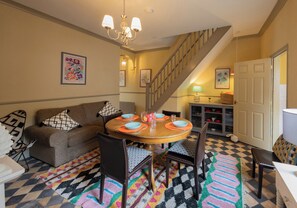 A dining area with a round table, chairs, a staircase, and a sofa. - No 2 Townhouse (Bishop Auckland)