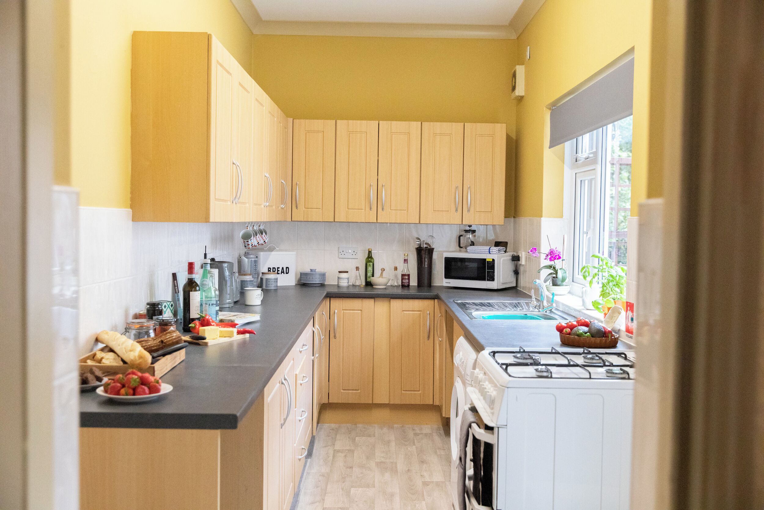 A kitchen with wooden cabinets, a microwave, a stove, and various food items on the counter.