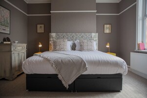 Un dormitorio con cama, lámparas de noche, cómoda y ventana.