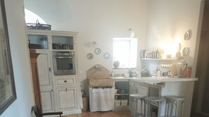 A dining area with a wooden table, chairs, and a kitchen in the background. - Maisonnette 80m2 for 3 15 km from Uzès (Lussan)