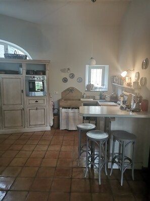 A kitchen with a stove, oven, sink, and stools. - Maisonnette 80m2 for 3 15 km from Uzès (Lussan)