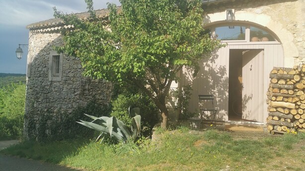 A stone building with a large tree in front, a door, and a stack of firewood. - Maisonnette 80m2 for 3 15 km from Uzès (Lussan)
