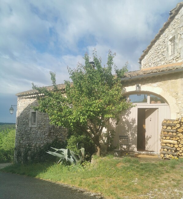 A stone building with a large tree in front, a door, and a stack of firewood. - Maisonnette 80m2 for 3 15 km from Uzès (Lussan)