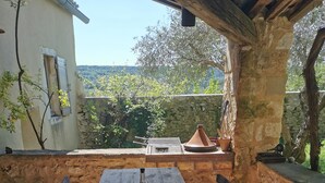 A rustic outdoor dining area with a wooden table and chairs, a bottle, and a view of the countryside. - Maisonnette 80m2 for 3 15 km from Uzès (Lussan)
