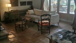 A cozy living room with a sofa, chairs, a table, and a large window with curtains. - Maisonnette 80m2 for 3 15 km from Uzès (Lussan)