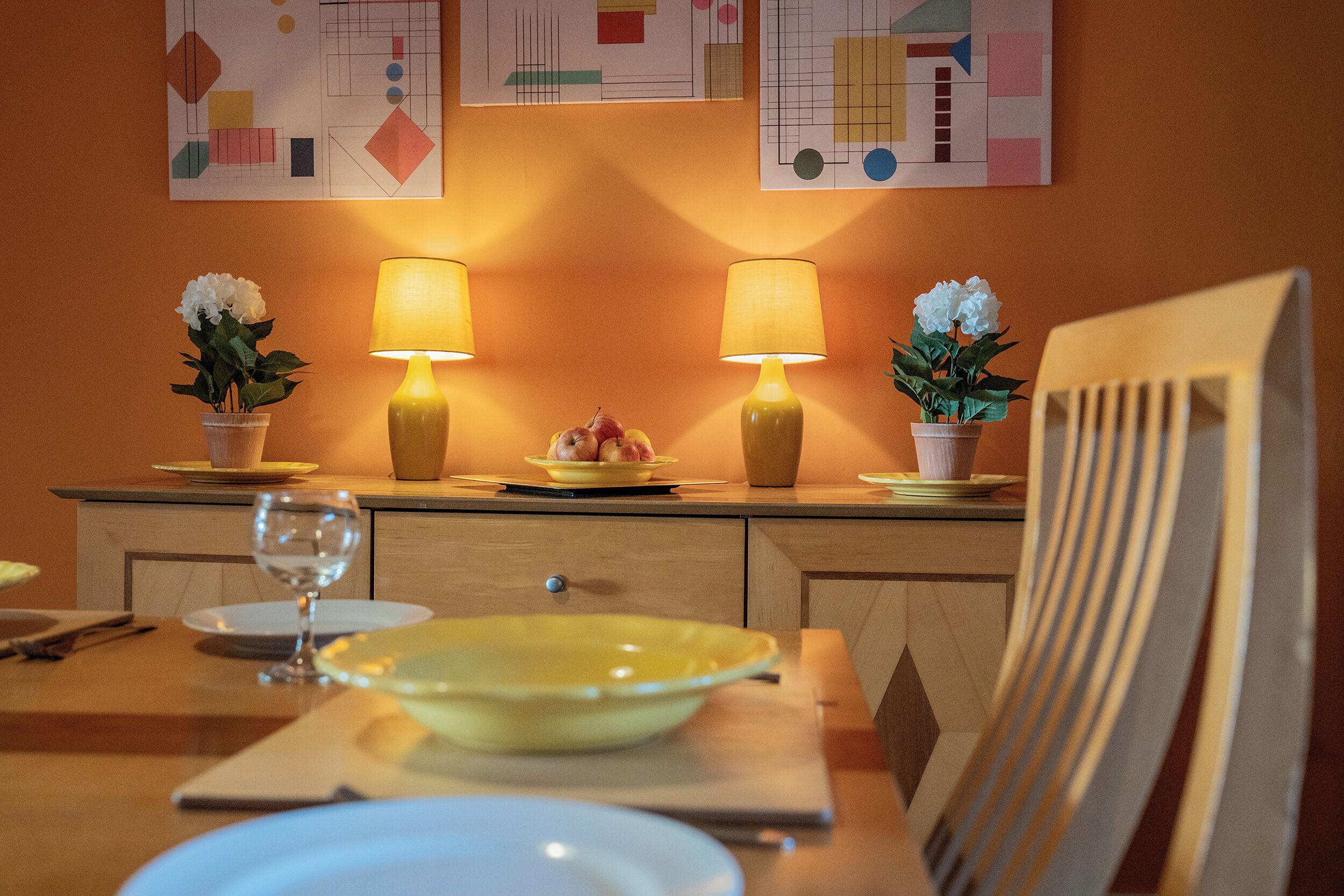 A dining table with yellow plates, two lamps, and potted plants.