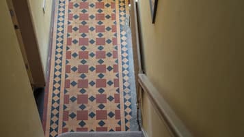 A narrow hallway with patterned floor tiles, a carpeted staircase, and walls with a simple design.
