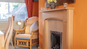 A room with a fireplace, a wicker chair, a small table, and a window with curtains.